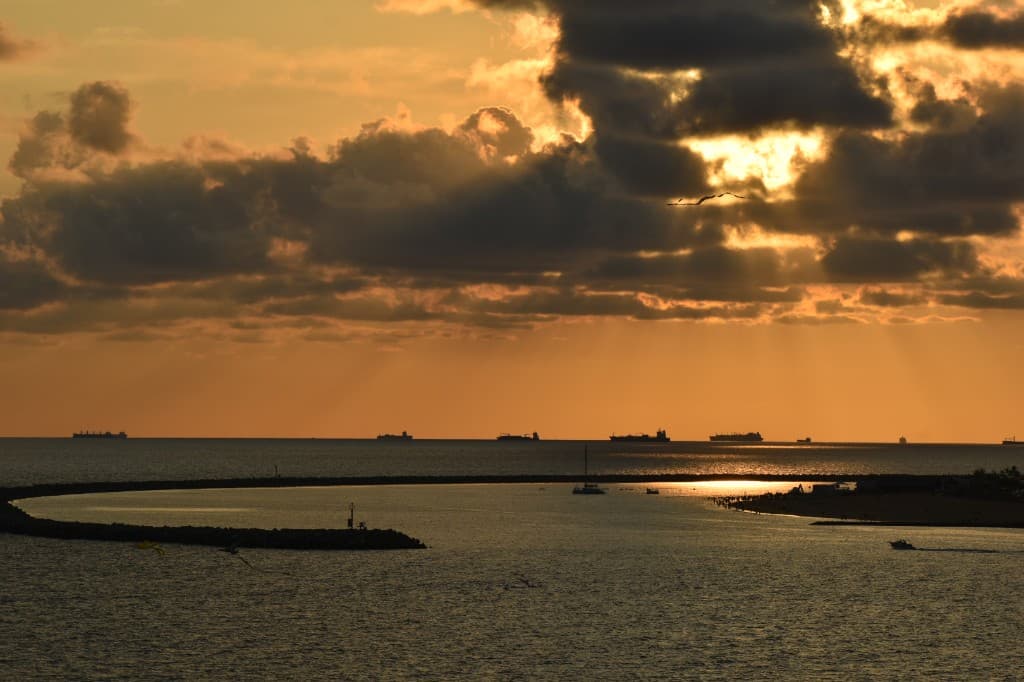 Sunset over a coastal harbor with cargo ships on the horizon and golden light through the clouds