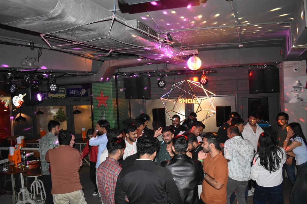 Crowded nightclub with colorful lights and a glowing Social sign above the dance floor